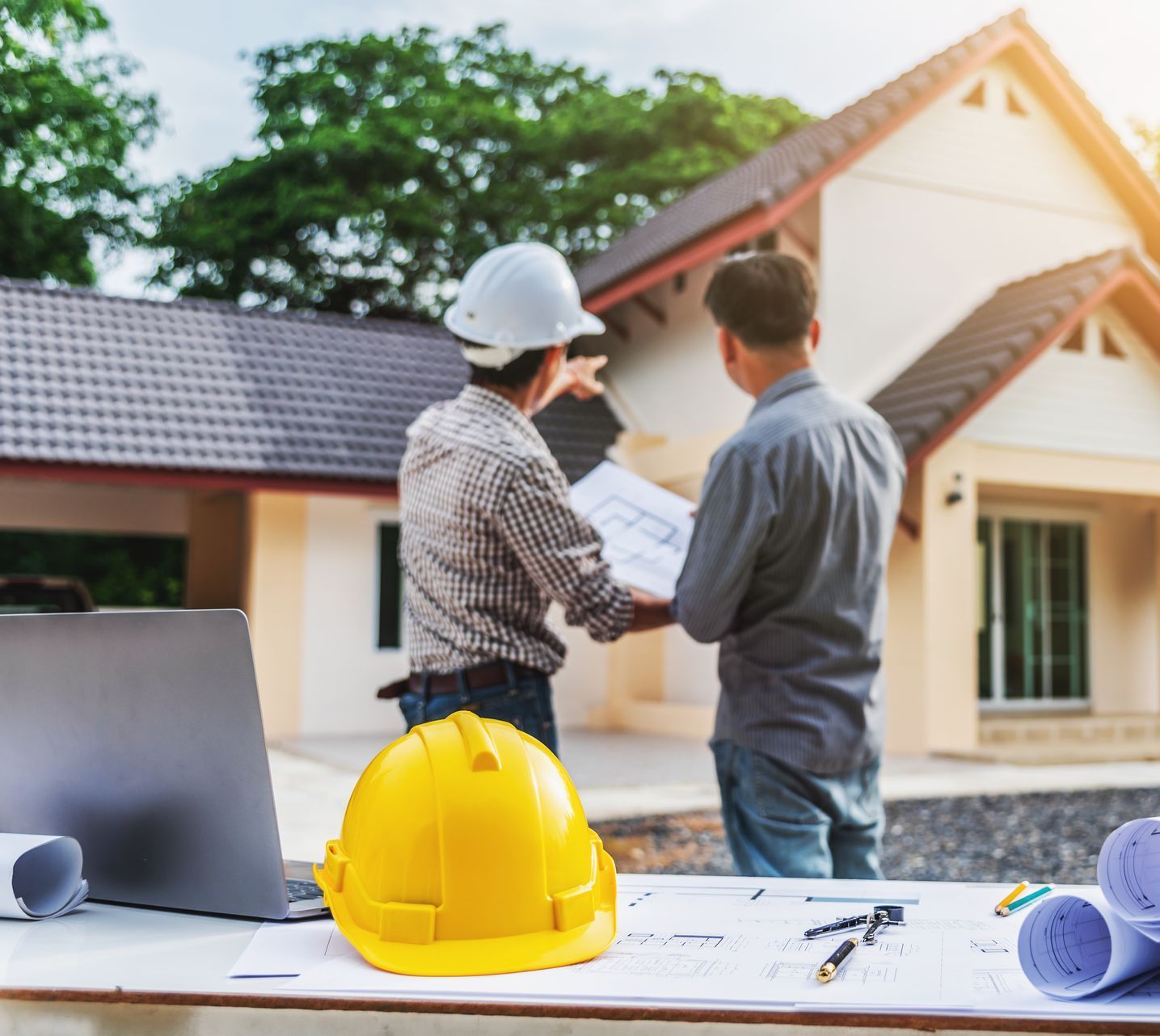 Two men are looking at a blueprint in front of a house.