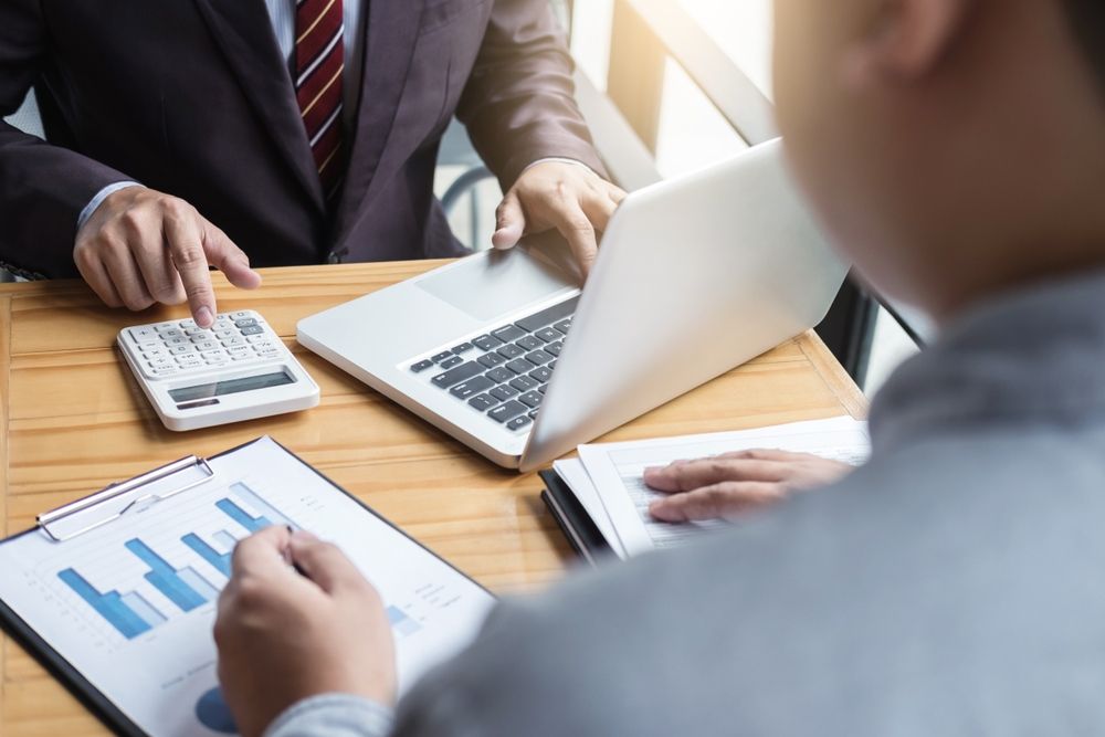Two Men Are Sitting At A Table With A Laptop And A Calculator — Tamworth Strata Management Services in Moree, NSW