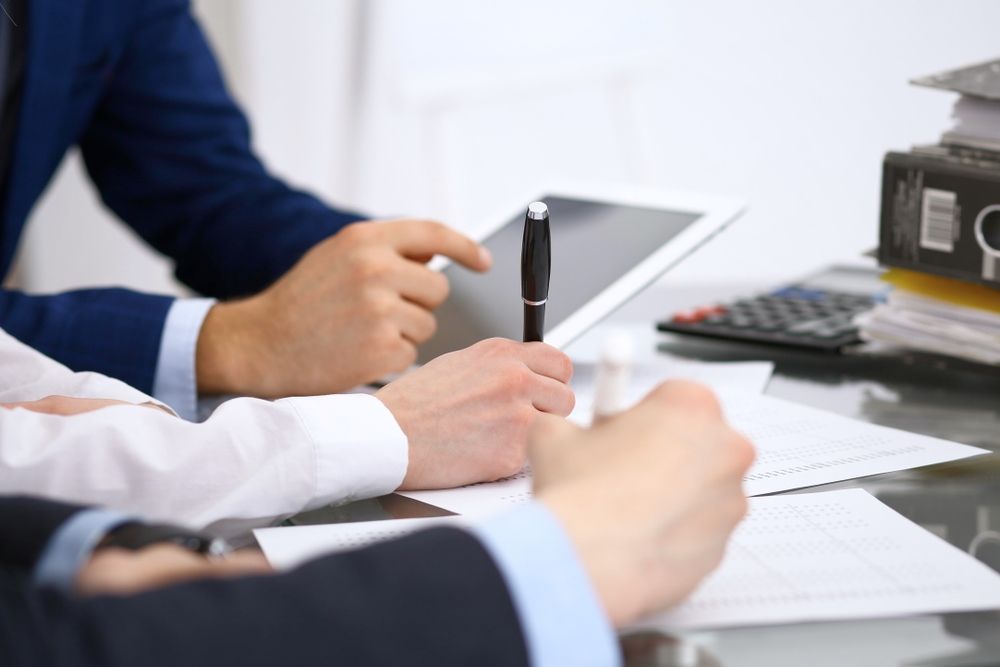 A Group Of People Are Sitting At A Table With Papers And A Tablet — Tamworth Strata Management Services in Moree, NSW