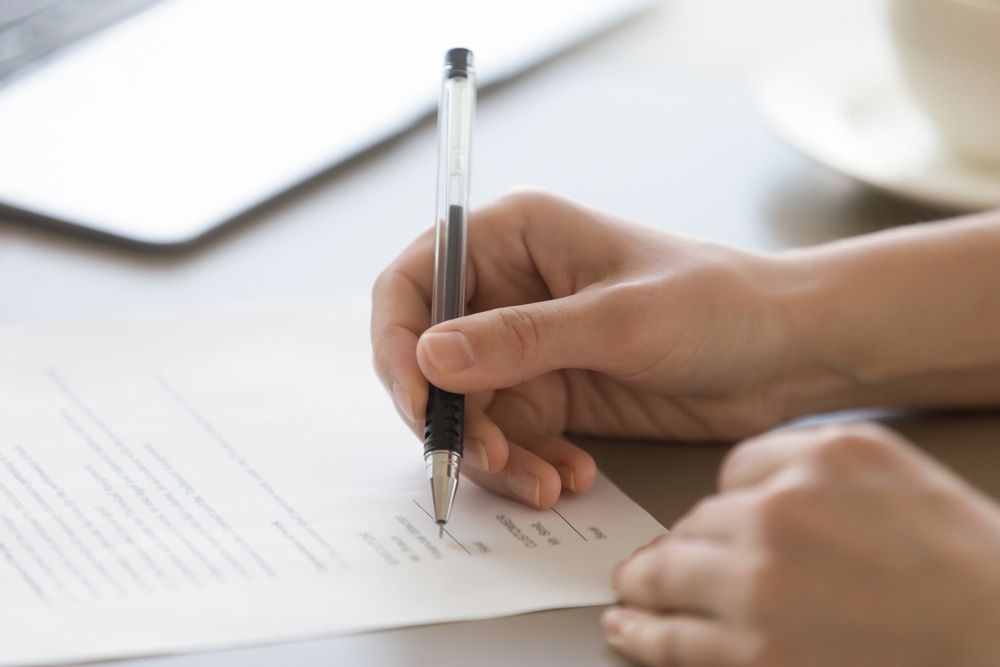 A Person Is Writing On A Piece Of Paper With A Pen — Tamworth Strata Management Services in Inverell, NSW