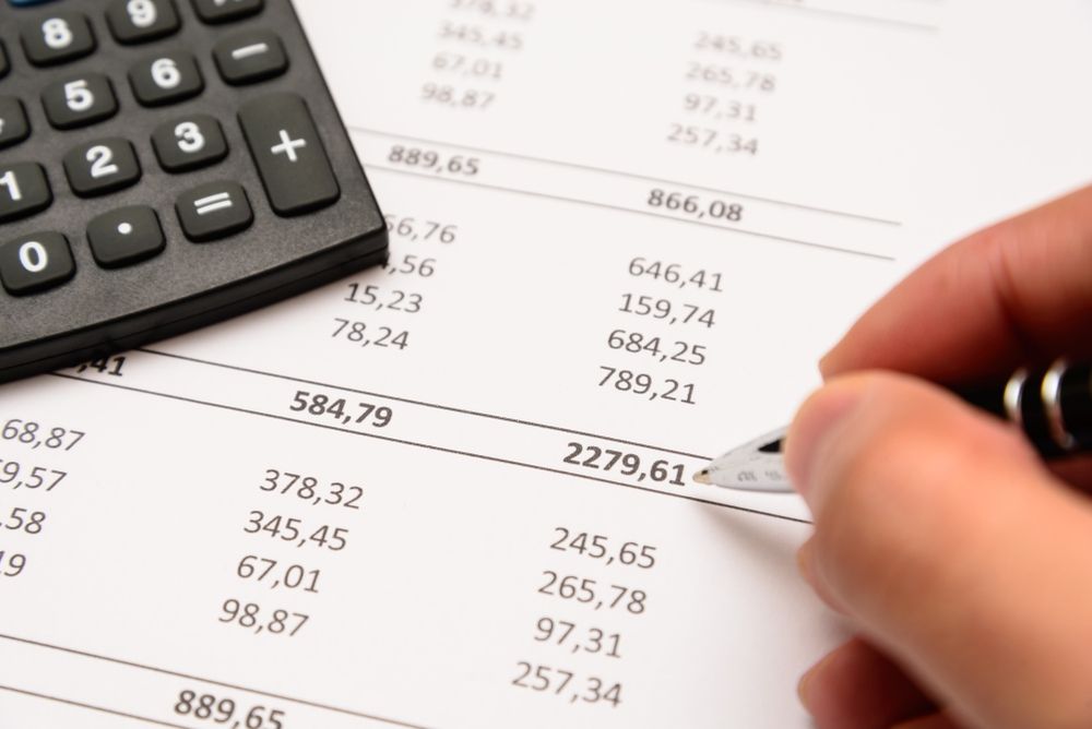 A Person Is Writing On A Piece Of Paper Next To A Calculator — Tamworth Strata Management Services in Inverell, NSW