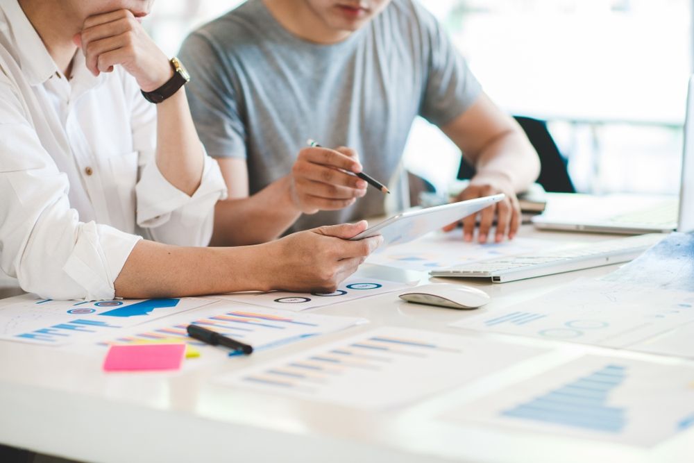 Two Men Are Sitting At A Table Looking At A Tablet — Tamworth Strata Management Services in Inverell, NSW