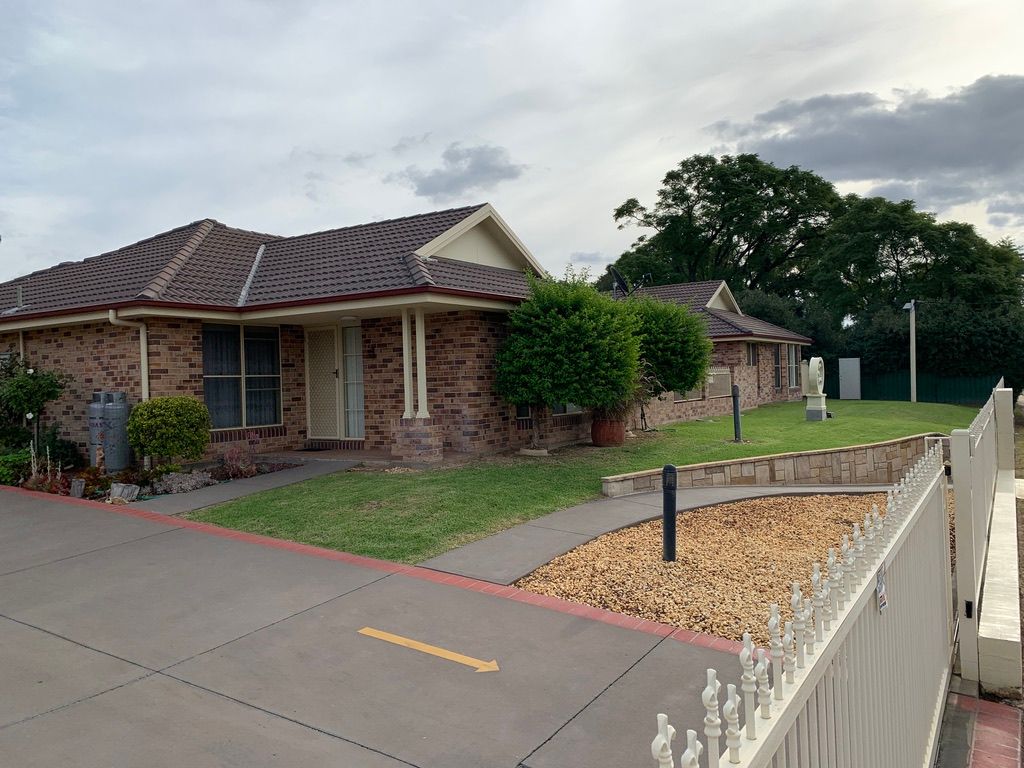 Brick house with a gray roof, green lawn, and white fence on a cloudy day. — Tamworth Strata Management Services in Gunnedah, NSW