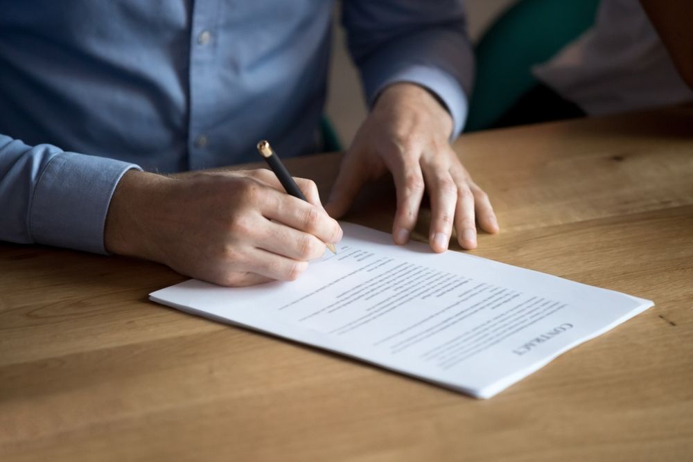A Man Is Signing A Document With A Pen On A Wooden Table — Tamworth Strata Management Services in Glen Innes, NSW