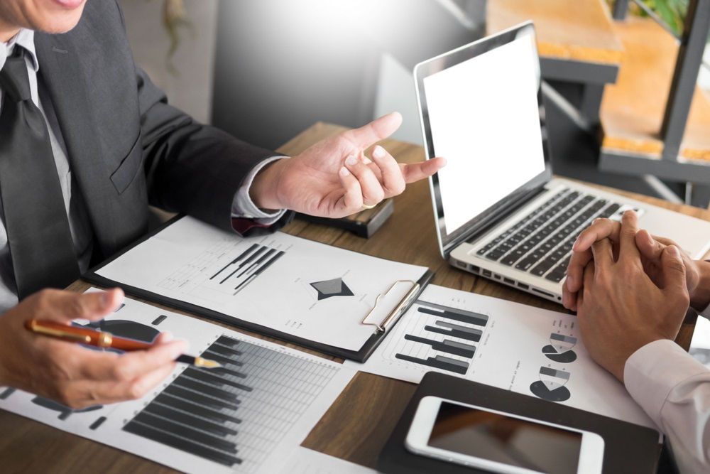 Two Men Are Sitting At A Table Looking At A Laptop Computer — Tamworth Strata Management Services in Glen Innes, NSW