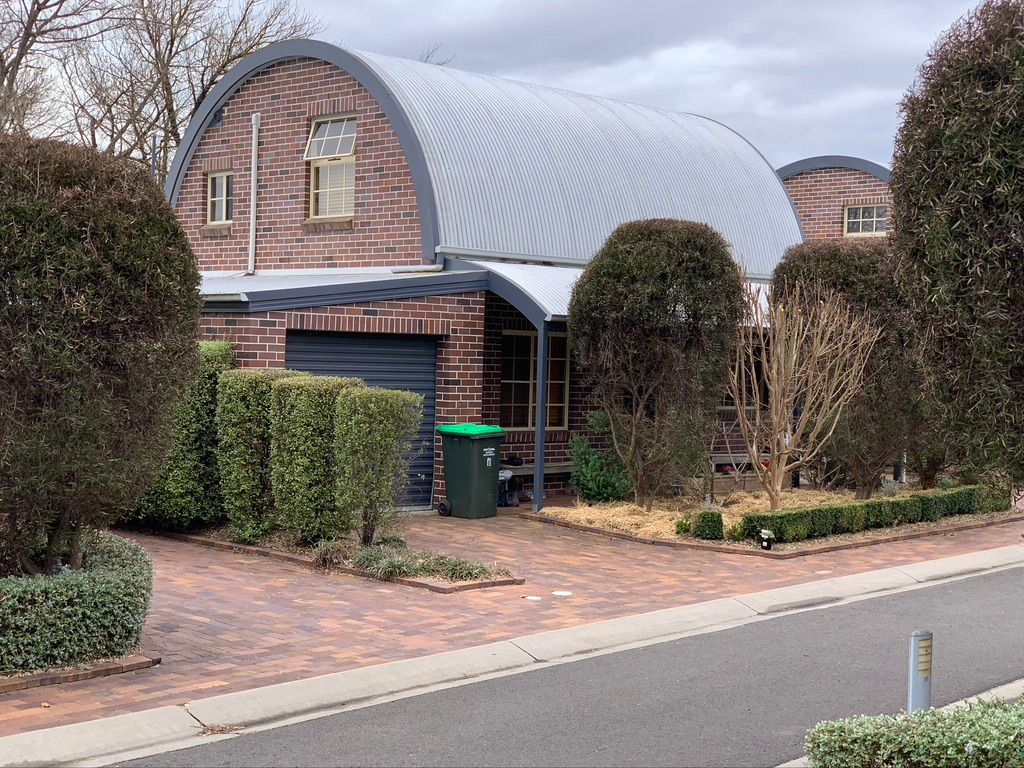 Brick house with arched metal roof, surrounded by shrubs and a brick driveway. — Tamworth Strata Management Services in Armidale, NSW