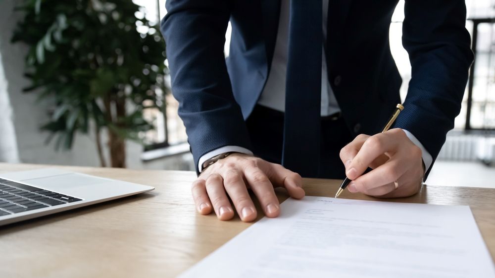 A Man In A Suit And Tie Is Signing A Document — Tamworth Strata Management Services in Scone, NSW