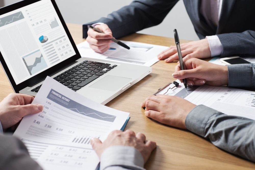 A Group Of People Are Sitting At A Table Looking At Papers And A Laptop — Tamworth Strata Management Services in Scone, NSW