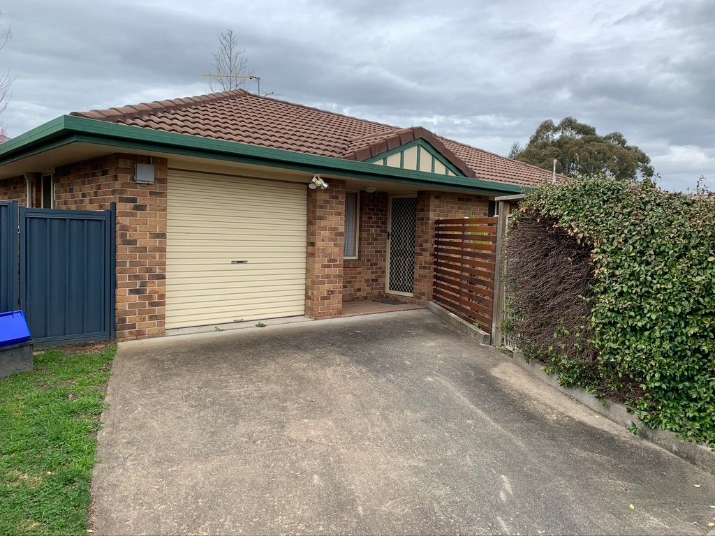 Brick townhouse with attached garage, concrete driveway, and green trim. Cloudy sky. — Tamworth Strata Management Services in Armidale, NSW