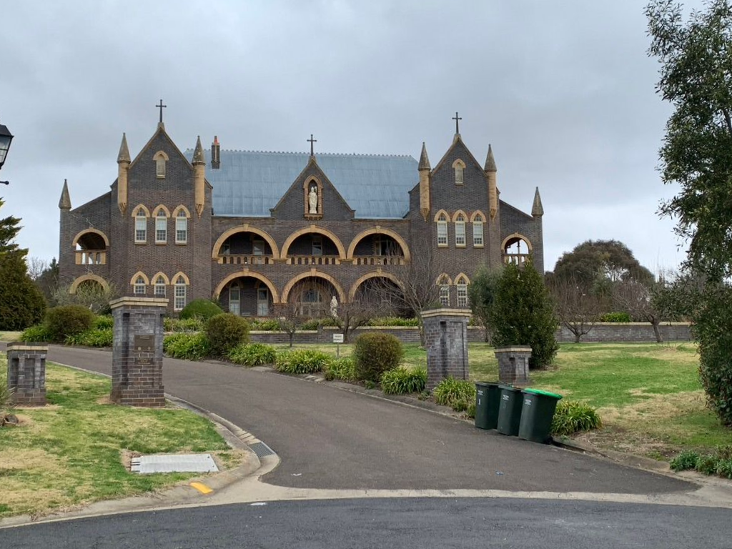 Historic brick building with arched windows, crosses, and a driveway, under a cloudy sky. — Tamworth Strata Management Services in Armidale, NSW
