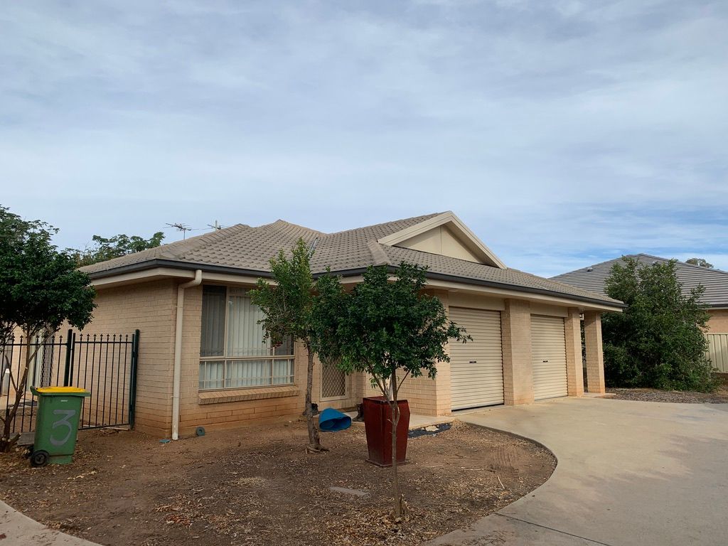Tan brick house with two garage doors and a green bin in front, under a cloudy sky. — Tamworth Strata Management Services in Gunnedah, NSW