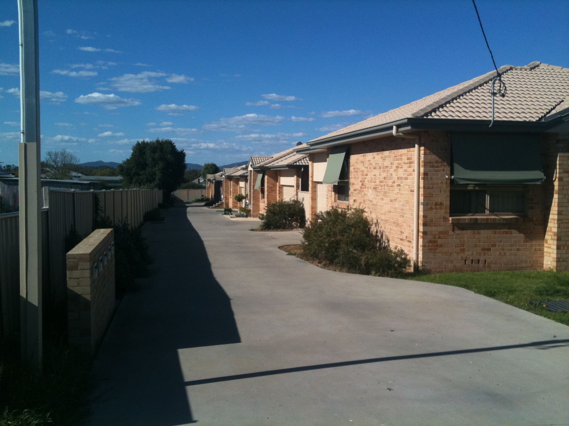 Row of brick townhouses with awnings, concrete walkway under a blue sky. — Tamworth Strata Management Services in Gunnedah, NSW