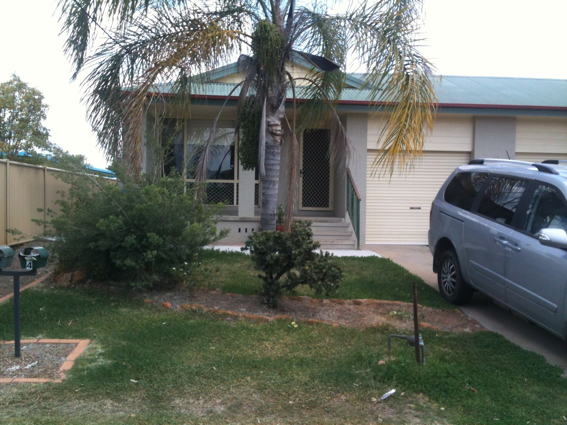 Front view of a single-story house with a minivan parked in the driveway and a palm tree in front. — Tamworth Strata Management Services in Narrabri, NSW