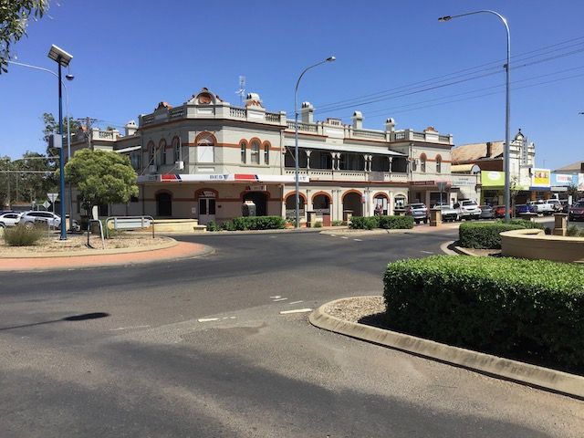 Street view of a two-story building with arched entryway, red brick accents, and a roundabout with cars. — Tamworth Strata Management Services in Narrabri, NSW