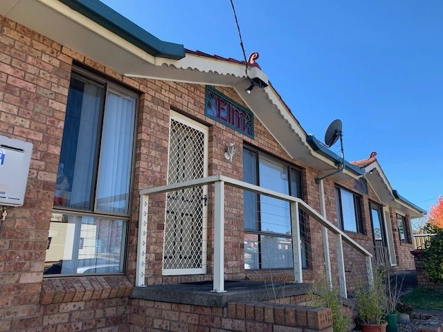 Brick building with multiple windows, front door, and a white railing. Sunny day. — Tamworth Strata Management Services in Glen Innes, NSW