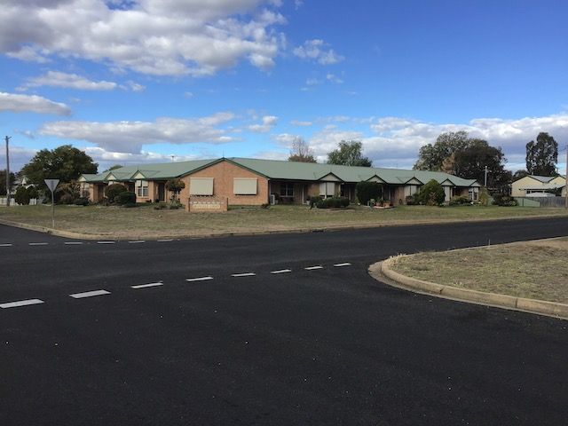A long, one-story brick building with a green roof sits at a street corner on a sunny day. — Tamworth Strata Management Services in Inverell, NSW