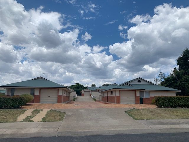 Row of brick houses with green roofs under a cloudy blue sky. — Tamworth Strata Management Services in Inverell, NSW