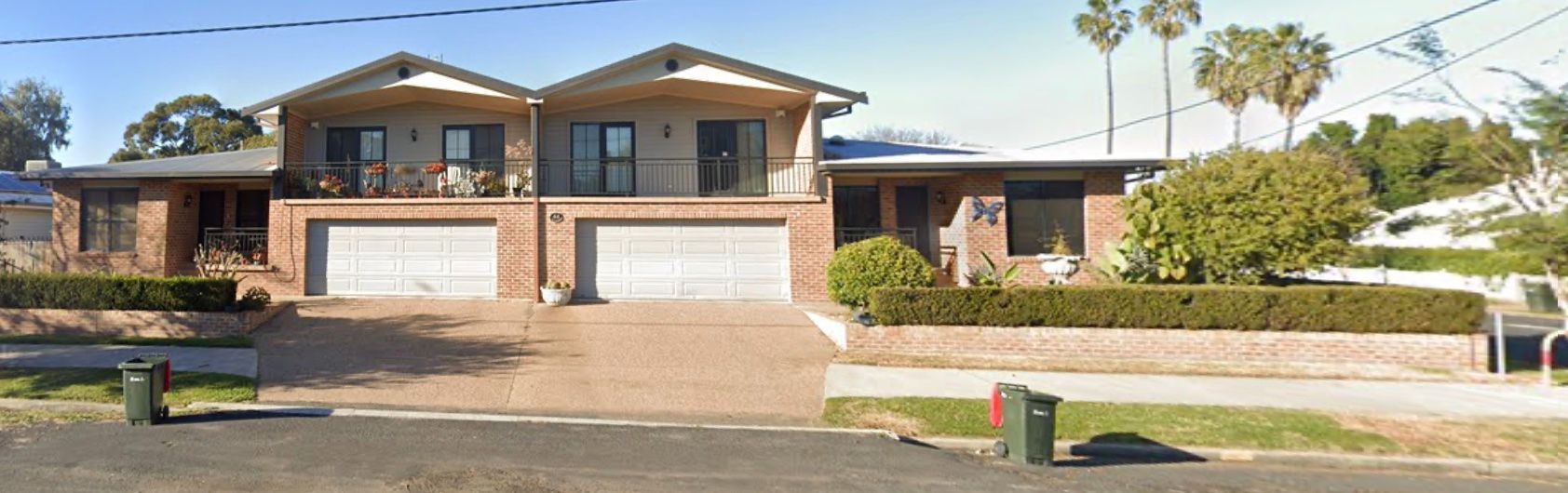 A multi-unit brick home with garage doors and balconies; two palm trees in the background. — Tamworth Strata Management Services in Moree, NSW