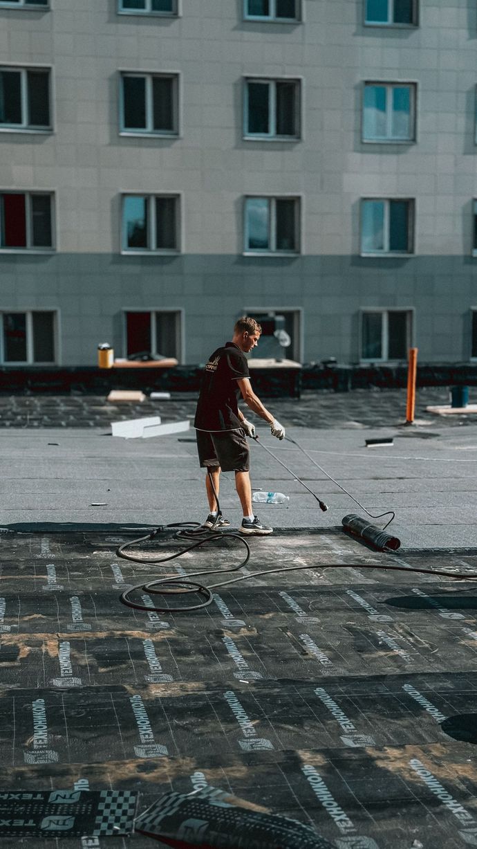 Roofers installing red clay tiles on a sloped roof, with legs and gloved hands visible.