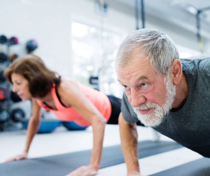 A man and a woman are doing push ups on a yoga mat in a gym.