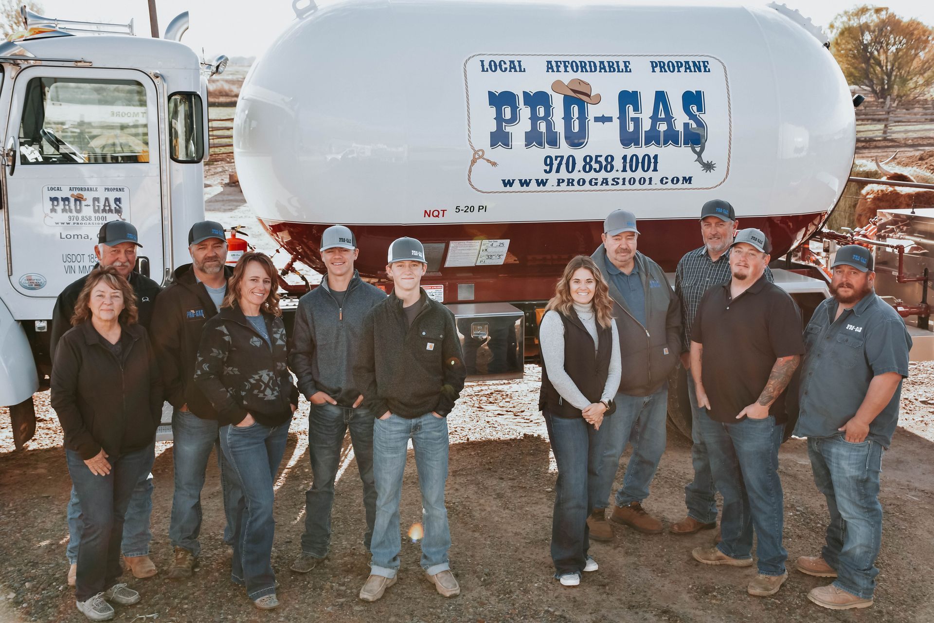 Pro-Gas company employees posing in front of a propane truck. All wear work clothes and smile.