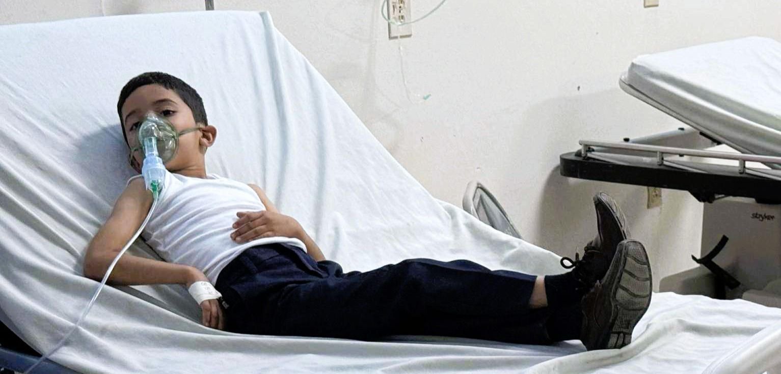 A child wearing an oxygen mask lies in a hospital bed.