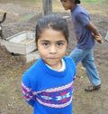Girl in a blue sweater with a decorative pattern, looking at the camera. Another person in background.