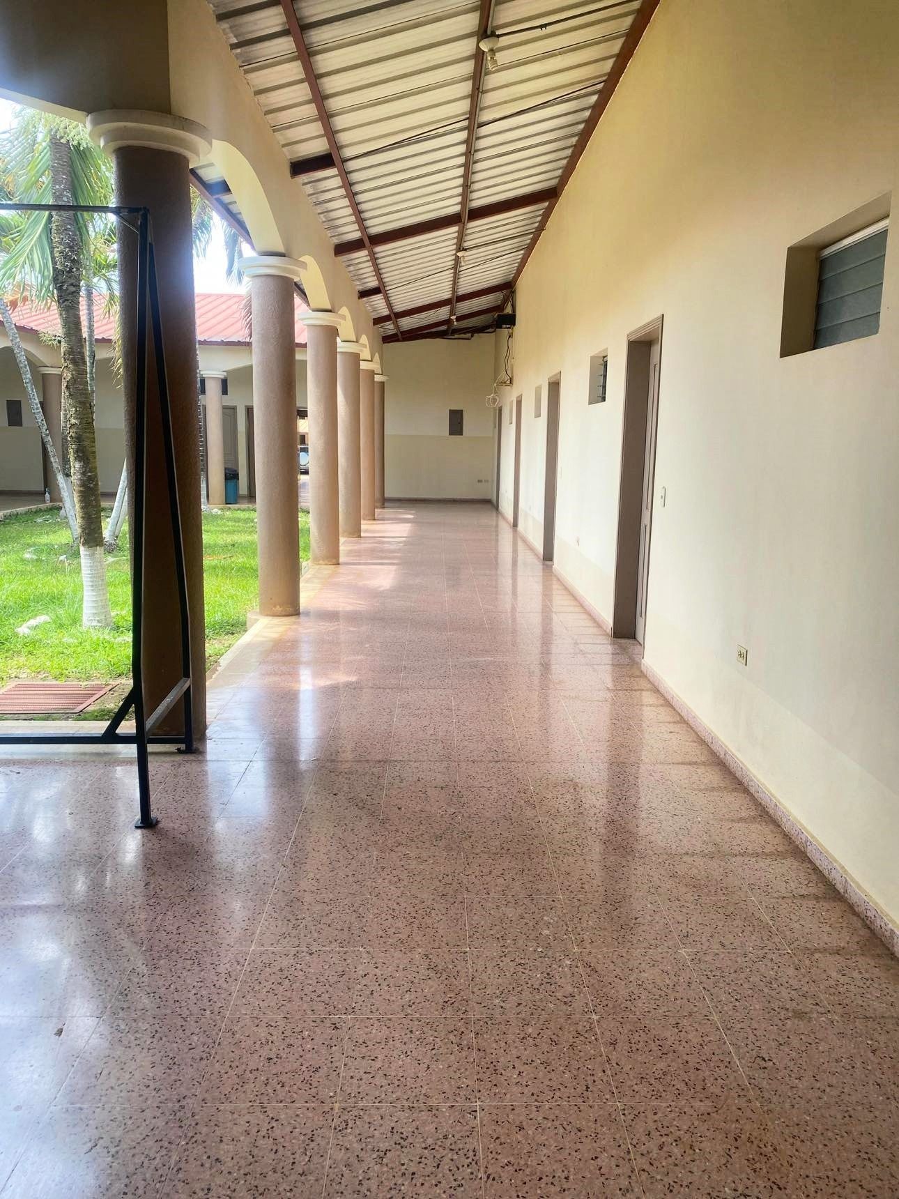 Long hallway with columns, doors, and a tiled floor. Exterior view with grass and trees visible.