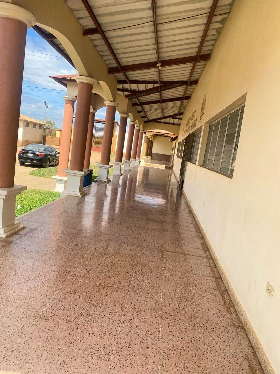 Long corridor with columns, brown and cream colors. Shiny speckled floor, windows, and a black car.