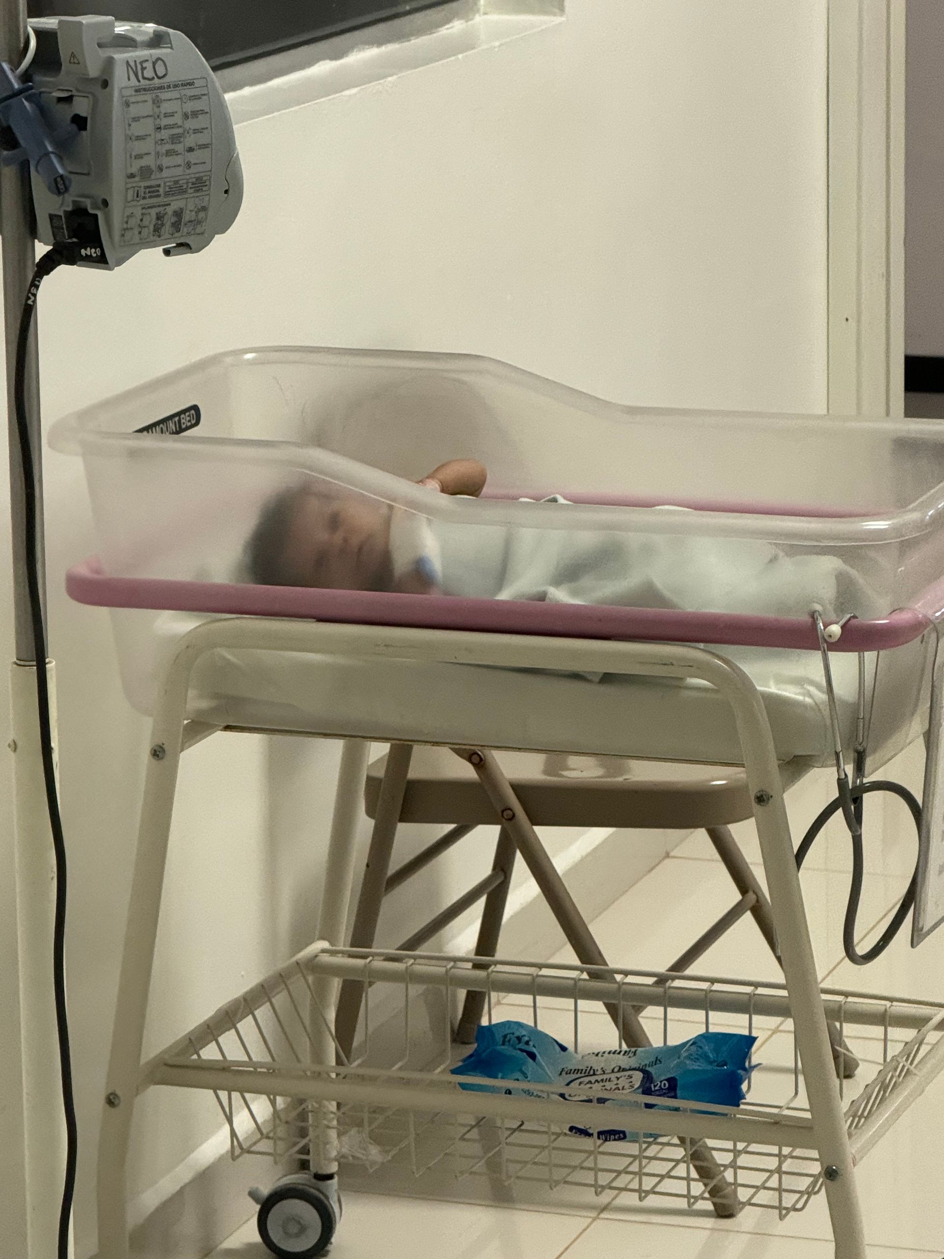 A newborn baby is laying in a clear crib