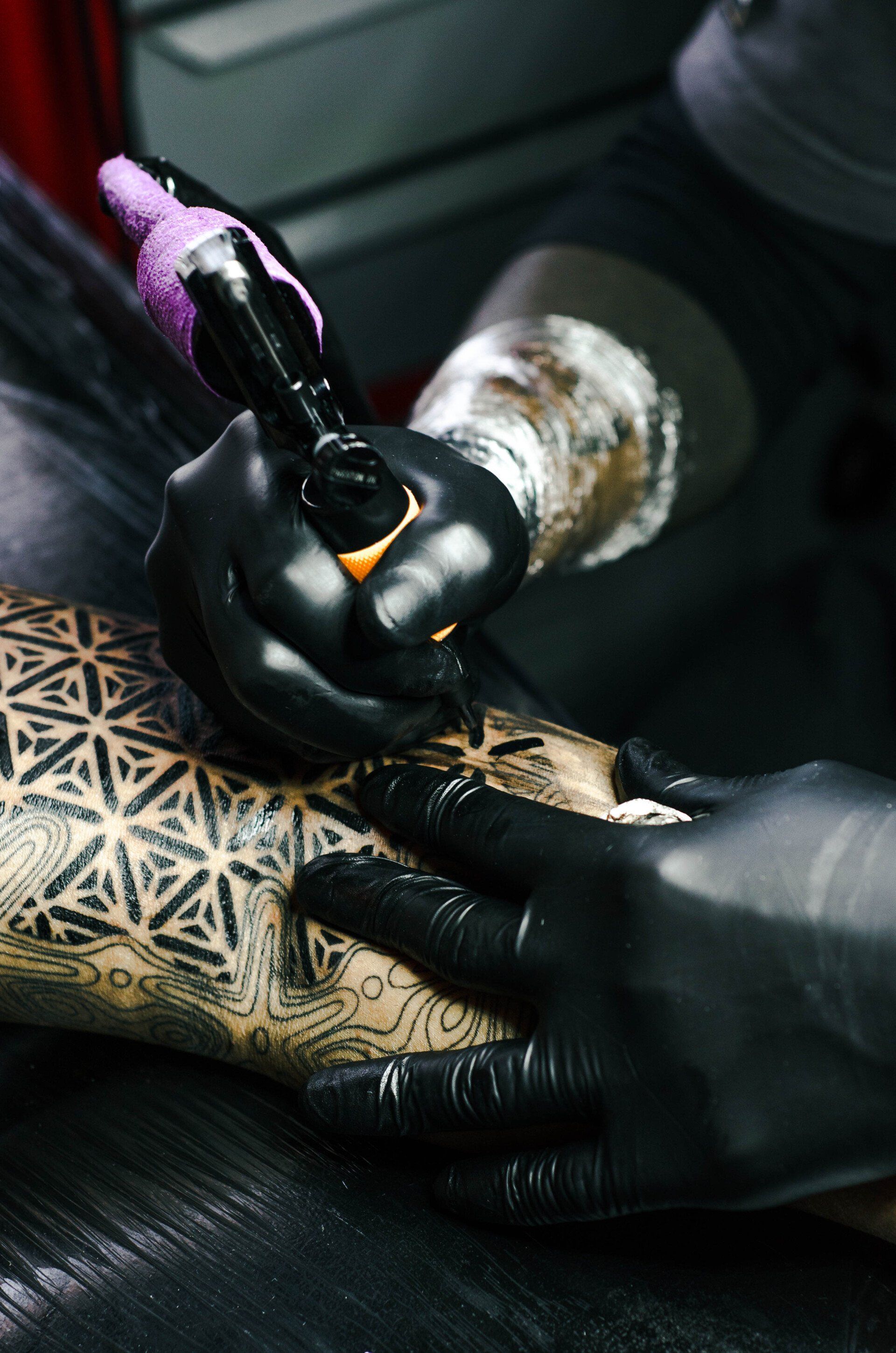 A woman is getting a tattoo on a man 's arm.
