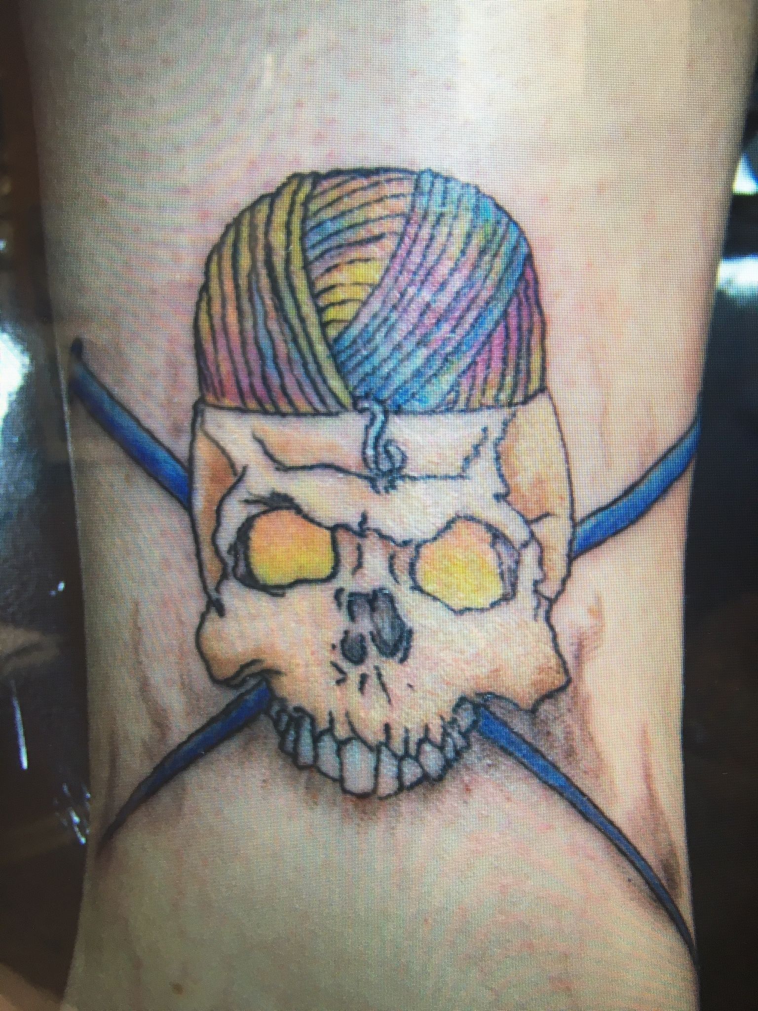 A tattoo of a skull with a ball of yarn on its head