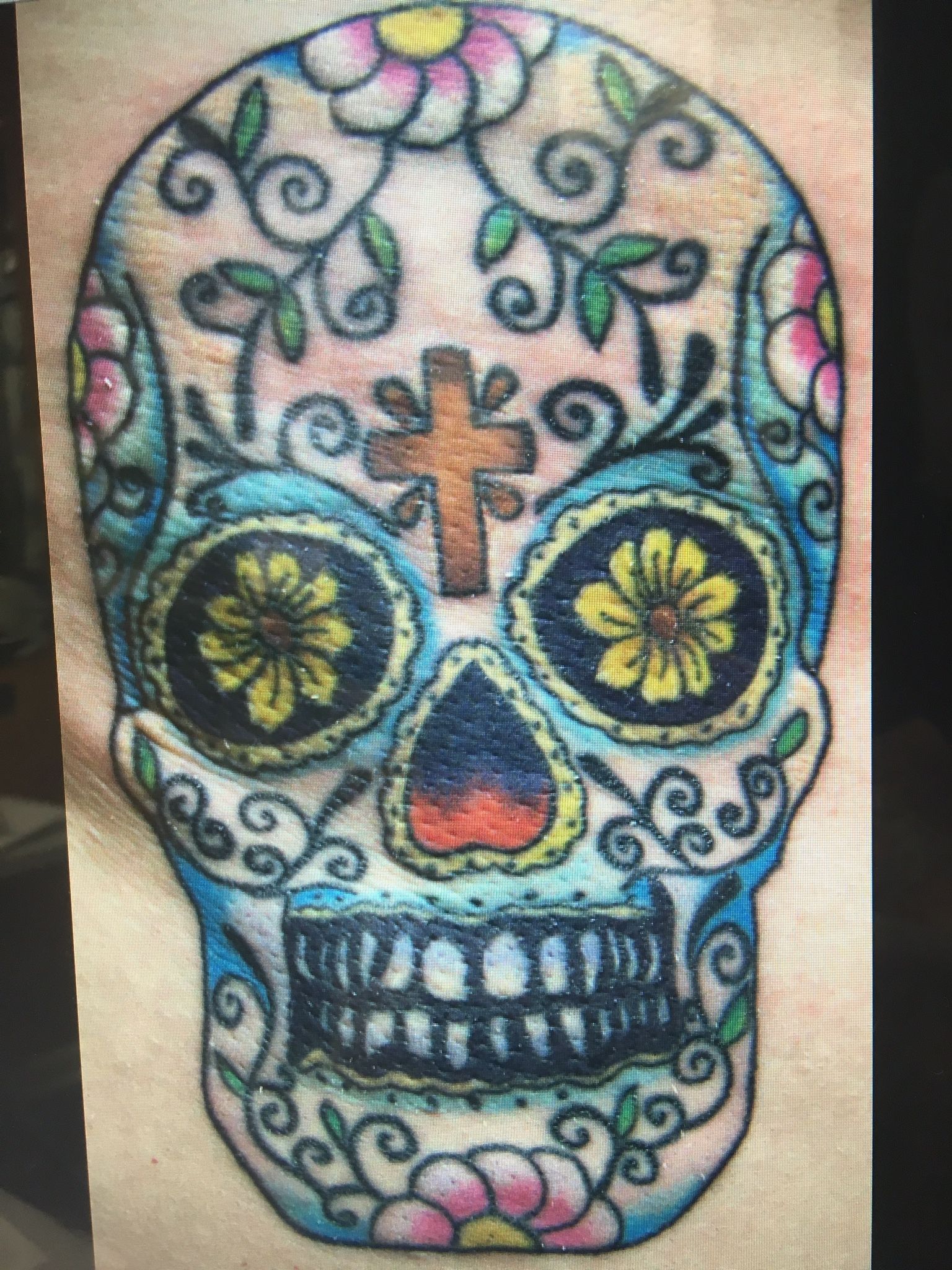 A sugar skull with flowers and a cross on it