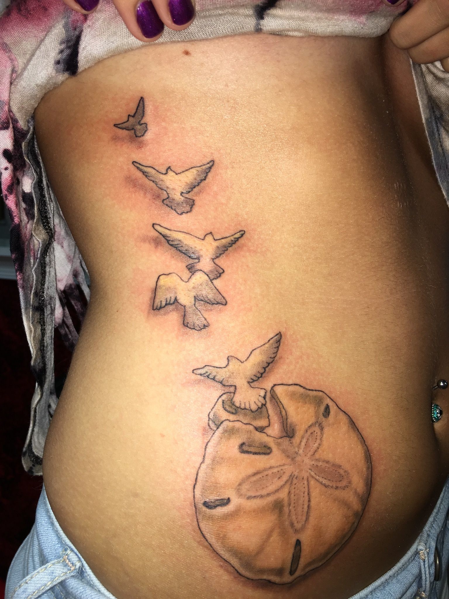 A woman has a tattoo of sand dollars and birds on her side.