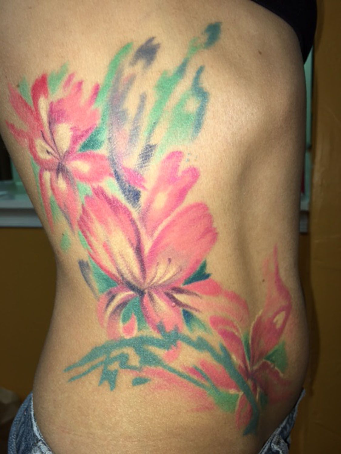 A woman has a tattoo of pink flowers on her back.