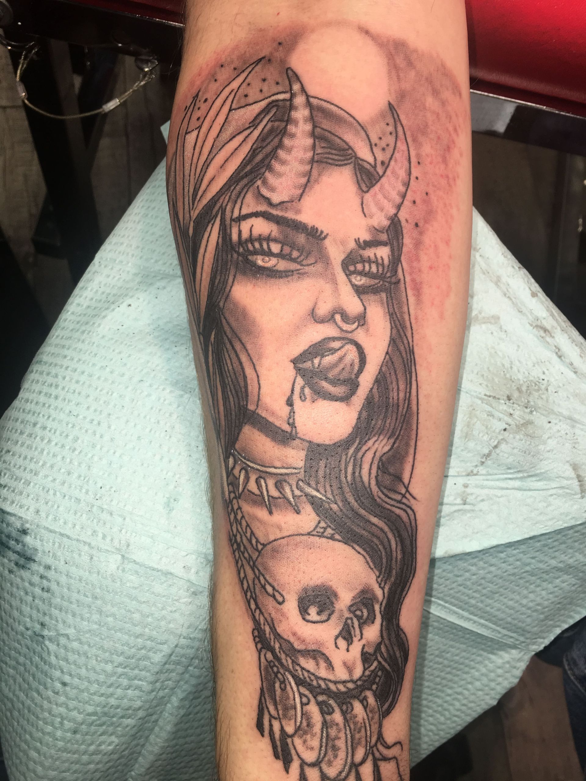 A tattoo of a woman with horns and a skull on her forearm.