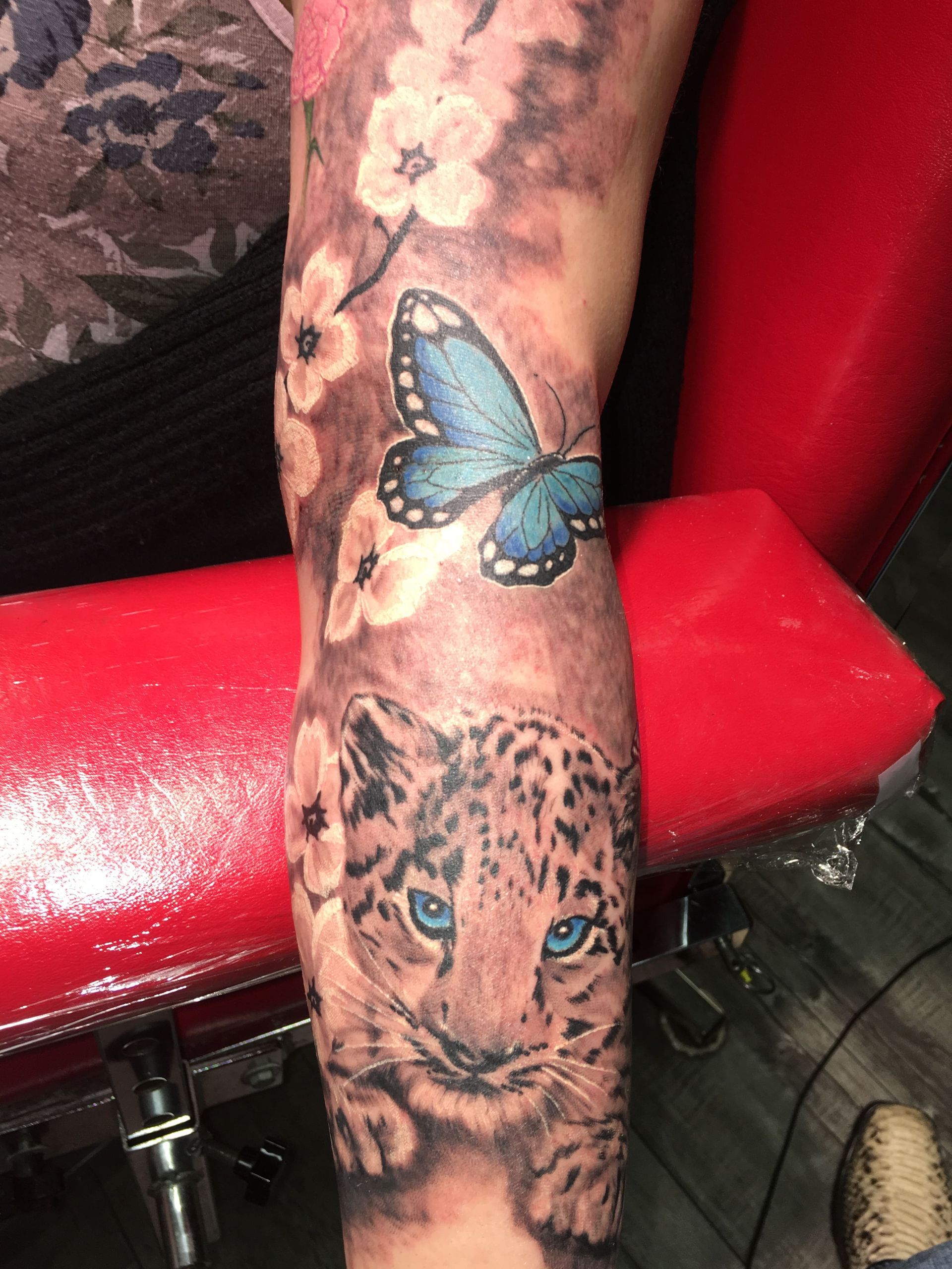 A person has a tattoo of a leopard and butterflies on their arm.