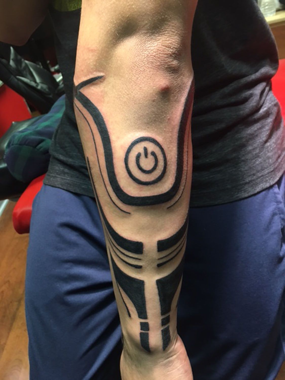 A man has a tattoo of a power button on his arm