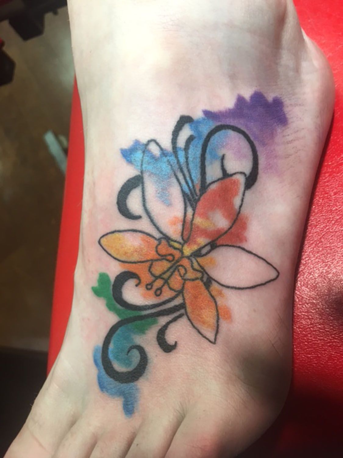 A person has a colorful flower tattoo on their foot