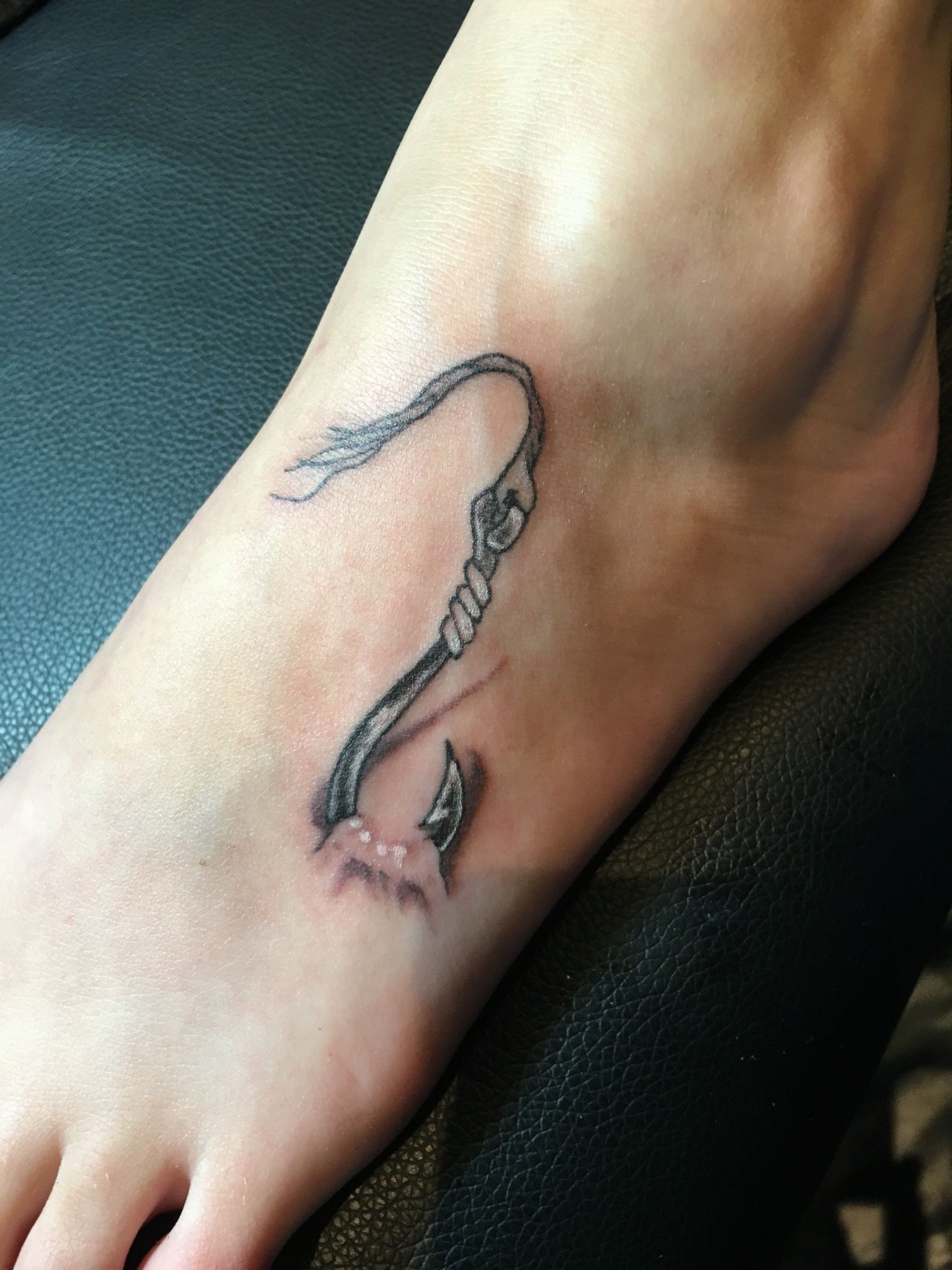 A person has a tattoo of a hook on their foot