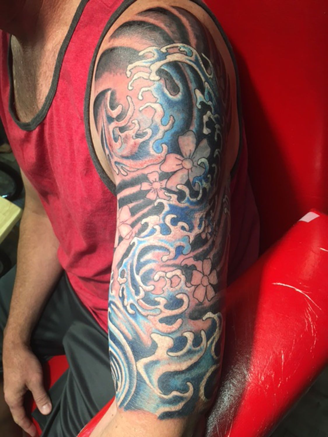 A man with a tattoo on his arm is sitting on a red chair.