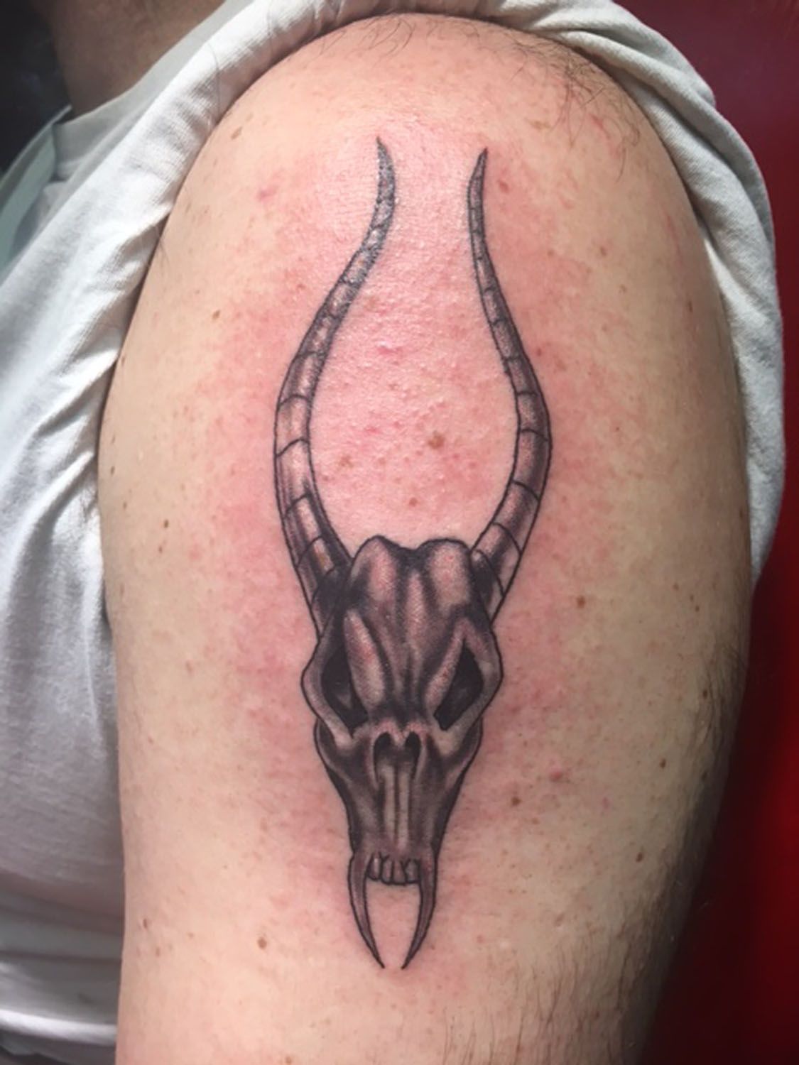 A man has a tattoo of a skull with horns on his shoulder.