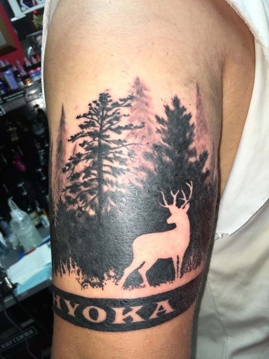 A tattoo of a deer in a forest with the name yoka