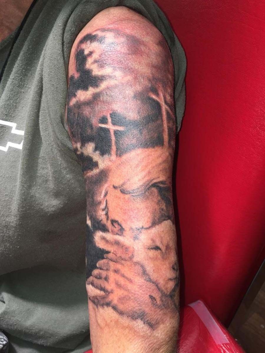 A man has a tattoo on his arm of a cross and a baby.