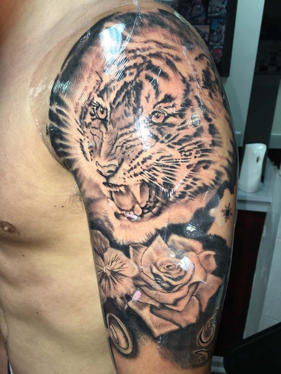 A man has a tattoo of a tiger and roses on his arm