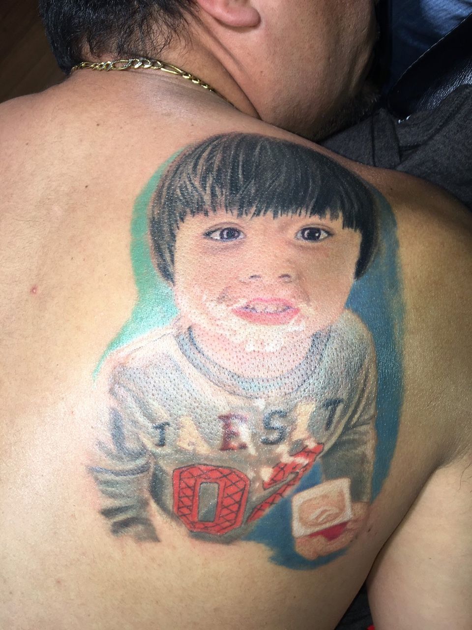 A man has a tattoo of a young boy on his back.