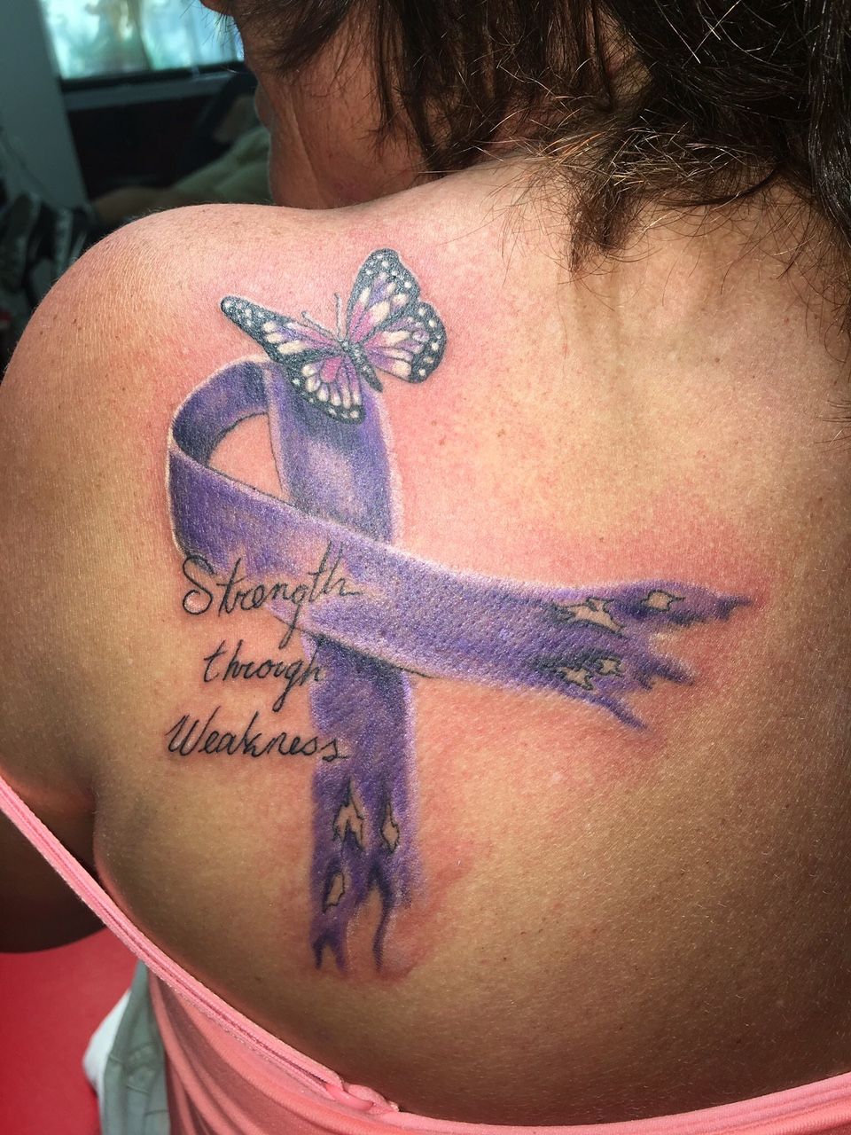 A woman has a tattoo of a purple ribbon and a butterfly on her back.