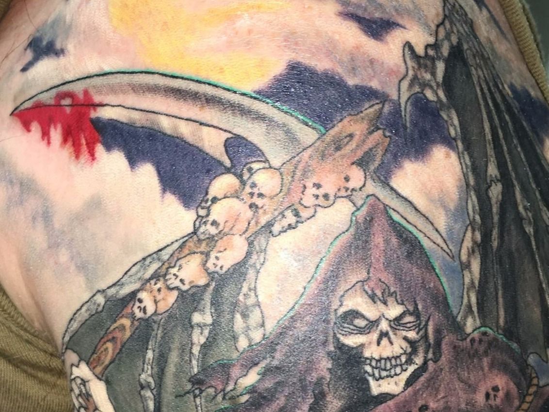 A tattoo of a grim reaper with a scythe and skulls on his chest.