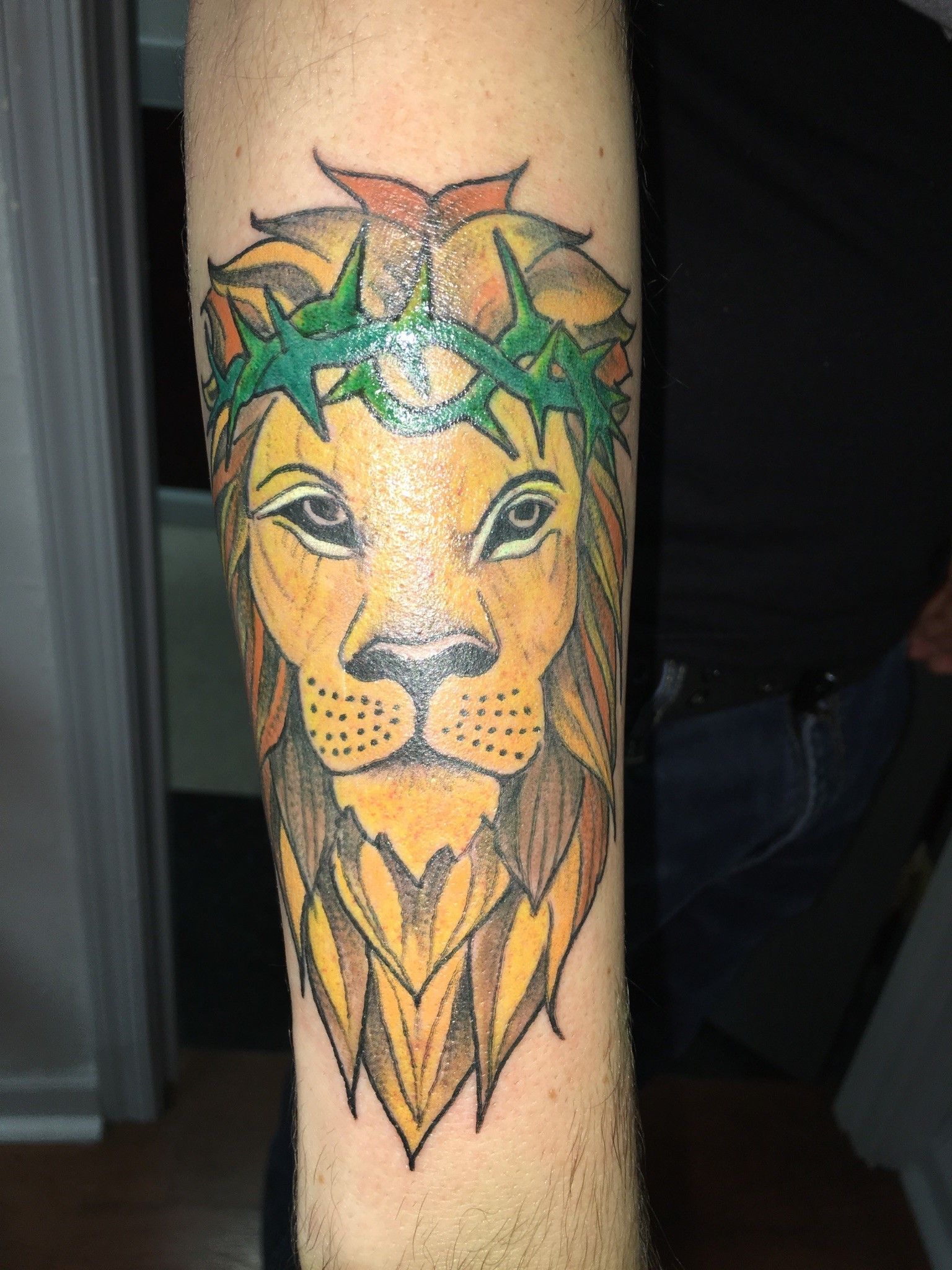 A man has a tattoo of a lion with a crown of thorns on his forearm.