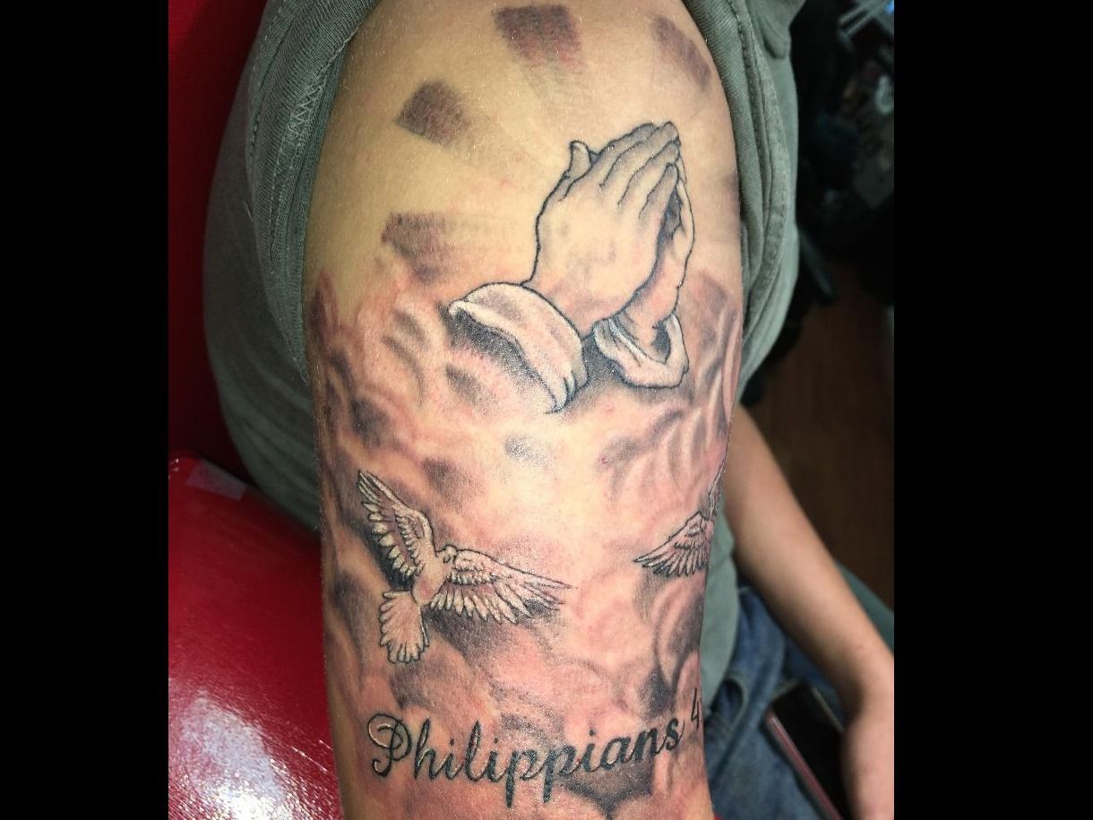 A man has a tattoo of praying hands and the name philippians